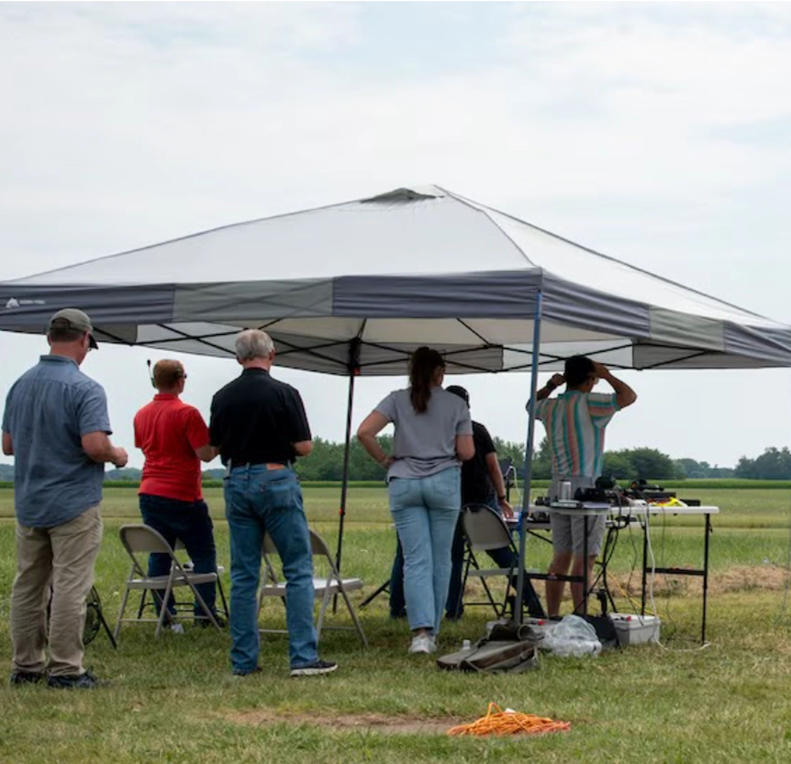 A group of people standing under a tent watching a Pivotal aircraft